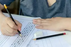 Students hand holding pencil writing selected choice on answer sheets